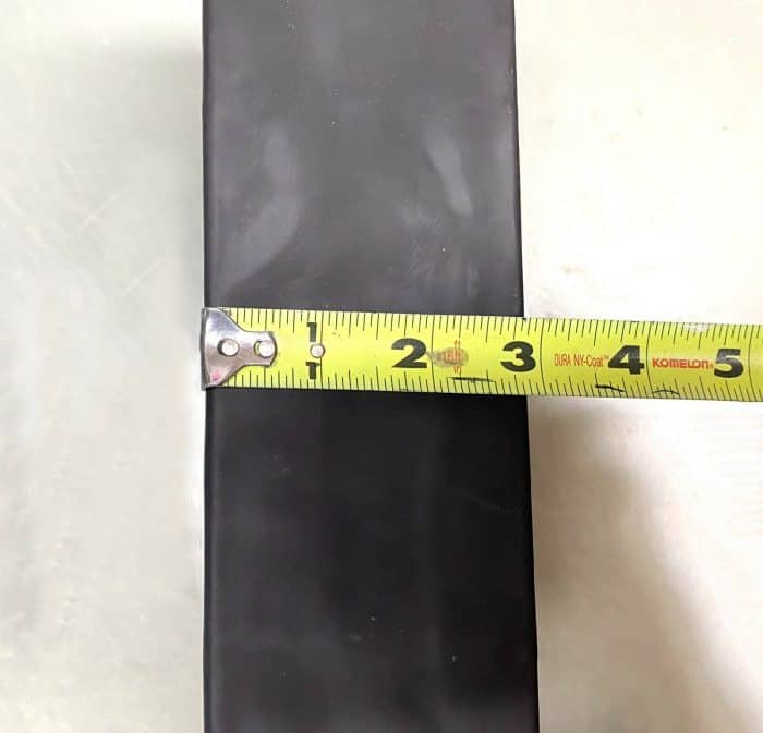 A tape measure is measuring the length of a black object.