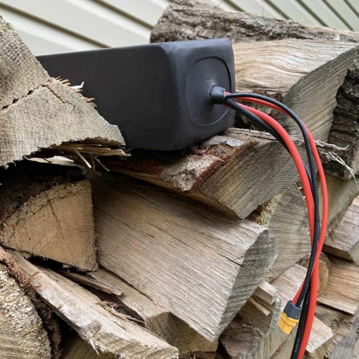 A black power cord plugged into the side of a pile of wood.