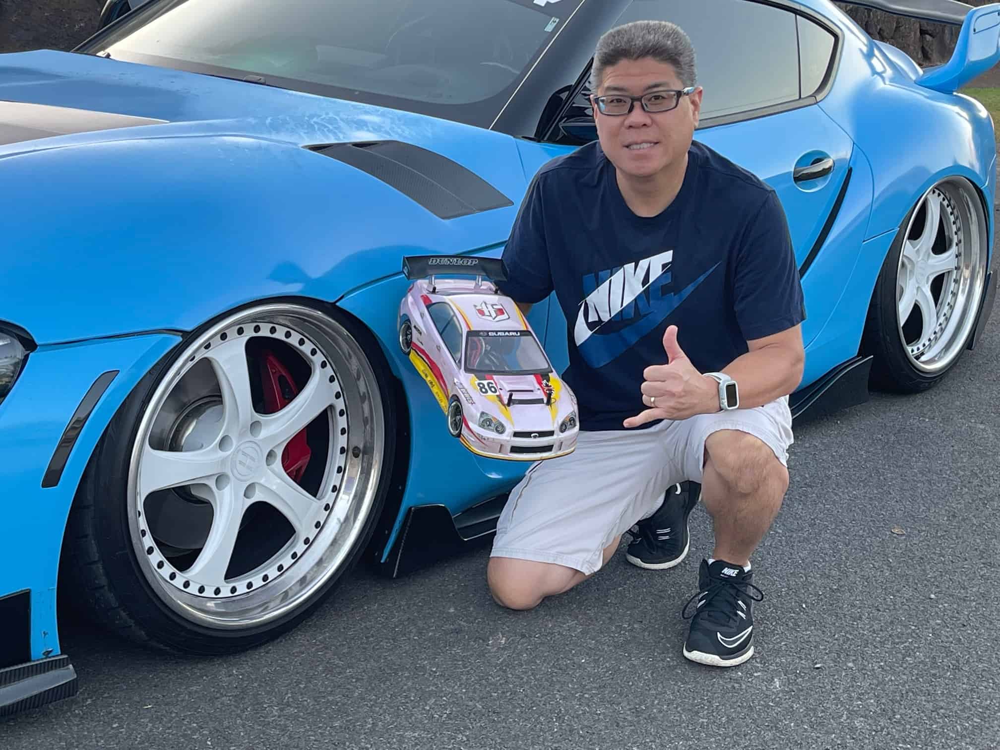 A man kneeling down next to a blue car.