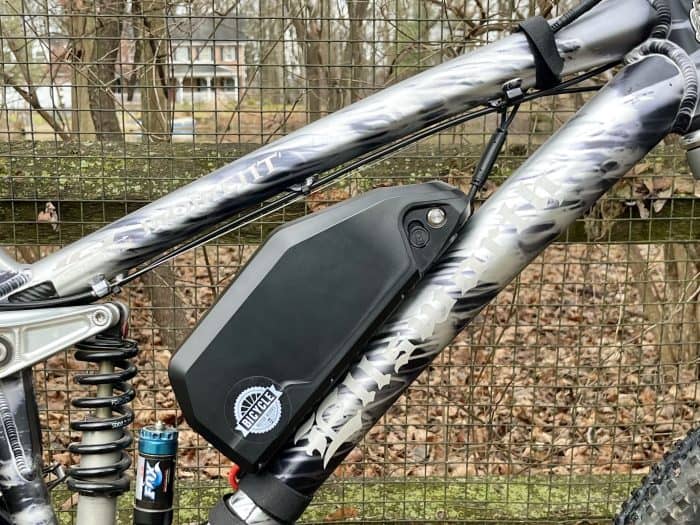 A bicycle with a black and silver frame is hanging from the side of a fence.